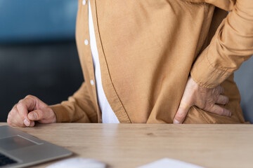 Man experiencing lower back pain while sitting at a desk, struggling with discomfort from prolonged...