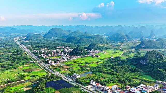 Aerial shot of the spectacular rural landscape with a highway, village, and green fields surrounded by karst mountains in southern China.