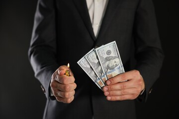 Man burning dollar banknotes on black background, closeup