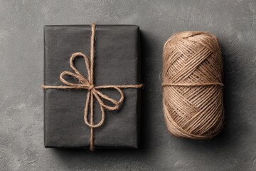 Dark gift box tied with twine, beside a ball of twine on a gray surface