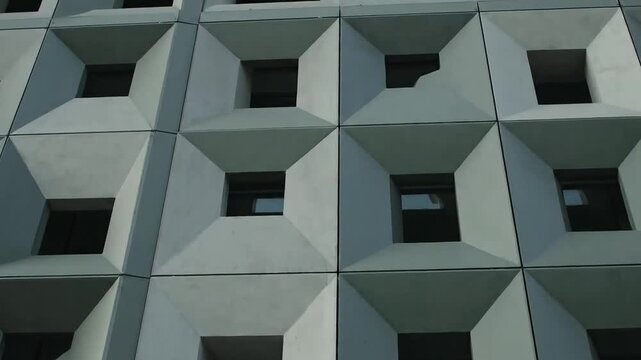 Geometric concrete facade with repeating square window openings creating abstract architectural pattern.