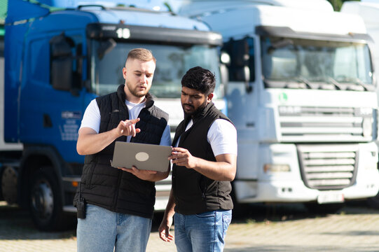 Truck drivers discussing logistics using laptop at fleet parking