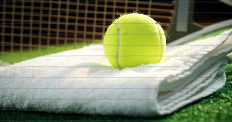 Resting tennis ball on white towel at tennis court, with orange tennis net, metal post