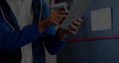 Holding tablet, technician wearing blue jacket tapping touchscreen in workshop, red stripe sign