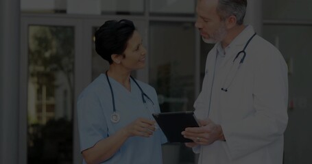 Doctor and nurse in uniform reviewing patient data at facility lobby, with tablet and stethoscopes