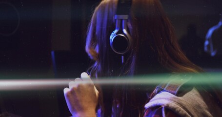 Singing recording artist wearing headphones and holding condenser mic in booth, light streaks