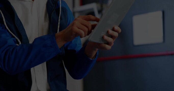 Holding tablet, technician wearing blue jacket tapping touchscreen in workshop, red stripe sign