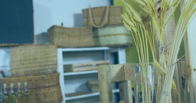 Displaying wheat stalks in clear vase at shop corner, baskets, bottles on shelving unit, copy space