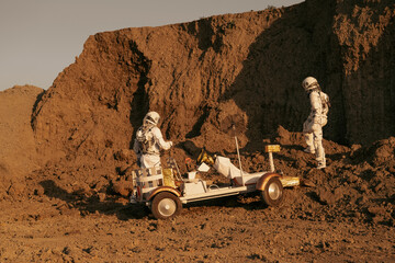 Space explorers examining a robotic rover on Martian terrain.