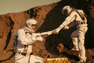 Astronaut reaching out a hand to help fellow crew member get up on the surface of Mars