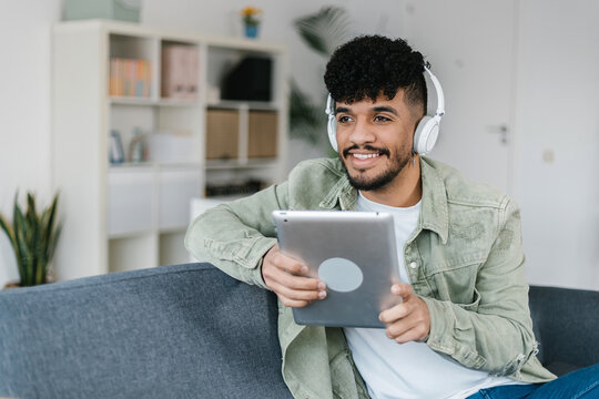 Millennial student boy holding digital device while sitting on couch. Young african american man using digital tablet relaxing on sofa at home