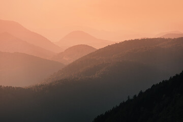 Mountain ranges receding into orange haze, creating a serene and peaceful natural landscape at sunset