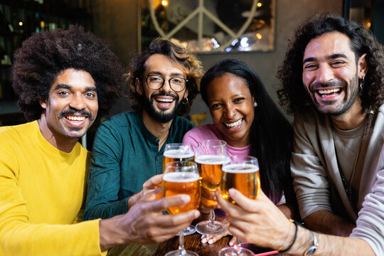 Cheerful multiracial friends are toasting and drinking beer in a bar, enjoying their time together - Powered by Adobe
