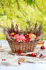 Florist at work: woman shows how to make seasonal autumn table decoration with pumpkins, flowers and plants in a wicker basket.