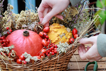 Florist at work: woman shows how to make seasonal autumn table decoration with pumpkins, flowers and plants in a wicker basket.