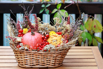 Florist at work: woman shows how to make seasonal autumn table decoration with pumpkins, flowers and plants in a wicker basket.