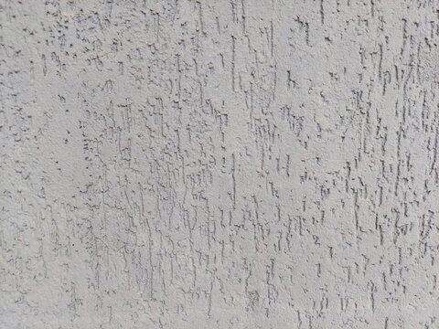 Close-up of an exterior wall featuring light gray textured plaster, often referred to as 'bark beetle' finish. The surface provides a rugged, neutral background.