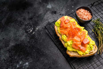 Toast with salty salmon, trout slices, avocado and red caviar. black background. top view