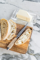 Sliced ciabatta bread with fresh butter on a wooden cutting board. marble background. top view