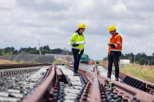 Two engineers wearing safety helmets and high-visibility jackets inspecting a railway track at a construction site.