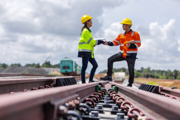 Two construction engineers wearing safety helmets and high-visibility jackets shaking hands on a railway construction site. Teamwork, project agreement, infrastructure development, industrial safety, 
