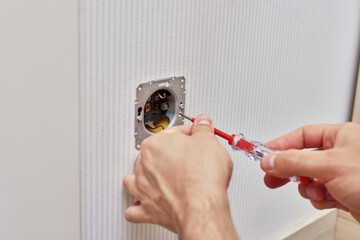 male hands installing electrical wall outlets with a screwdriver at home
