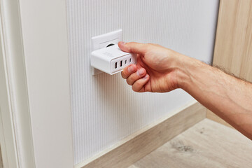 male hand insert a plug of the phone charger into socket at home