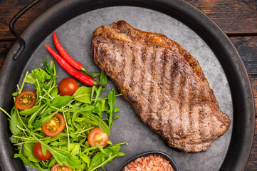 Grilled striploin steak, strip loin beef meat steak on a steel tray. wooden background. top view