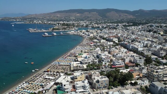 Aerial view of the vibrant beach meeting the turquoise sea, alongside the bustling harbor of Kos, a captivating blend of nature and urban life, Kos, Greece.