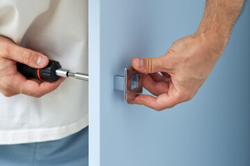 worker installing handle of blue cabinet door with screwdriver, close-up. furniture assembly service