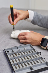 female hands with screwdriver repairing kids toy on grey table. repair shop, focus on screwdriver set