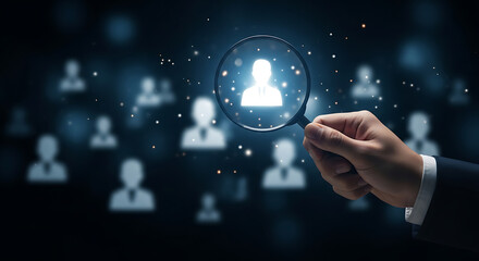 Fototapeta premium Hand holding magnifying glass over a highlighted business person silhouette, representing recruitment, talent search, and selection process