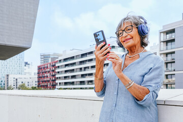 Senior woman enjoying music using smartphone in city