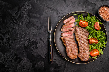 Grilled Steak from Black Angus beef meat on a plate with salad. black background. top view
