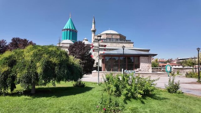 Mevlana Rumi Museum building in Konya, Turkey with a distinctive green dome surrounded by lush greenery. Sunlight enhances the vibrant colors, creating a serene atmosphere.