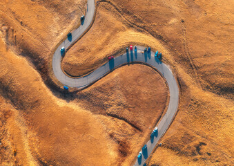 Aerial view of winding road in mountain pass at sunset in golden autumn. Passo Giau, Dolomites, Italy. Beautiful curving roadway, cars, orange grass, alpine meadows. Landscape with highway in fall