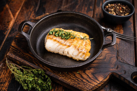 Roasted cod fish loin fiilet in skillet. Wooden background. top view