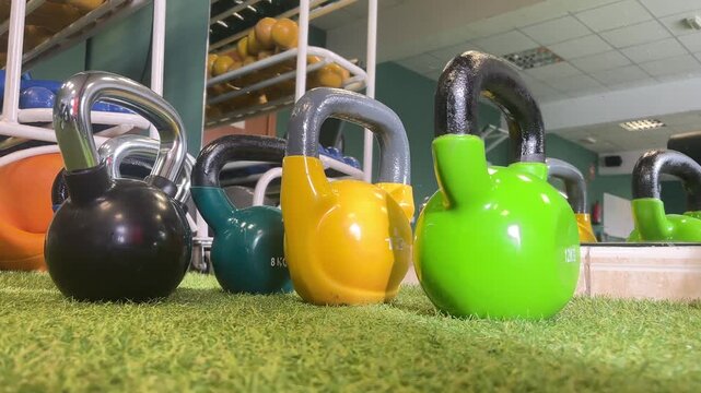 A row of colorful kettlebells are lined up on a green and yellow one that is labeled 12.5