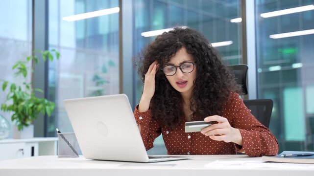 Upset shocked businesswoman detected fraud checking credit card on computer sitting in business office. Angry annoyed female employee became victim of deception, money was stolen from her account