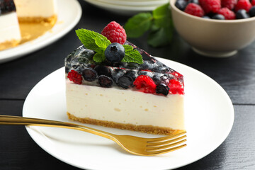 Piece of delicious cheesecake with berries and mint on black wooden table, closeup
