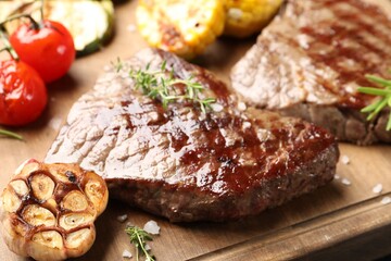 Delicious grilled beef steaks with herbs and vegetables on wooden board, closeup