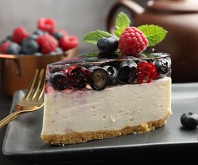 Piece of delicious cheesecake with berries, mint and fork on table, closeup