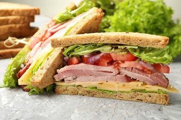 Delicious sandwiches with ham, cheese and vegetables on grey textured table, closeup