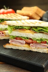 Tasty sandwiches with ham, bacon, cheese and vegetables on wooden table, closeup