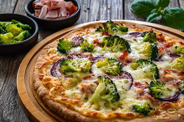Pizza with bacon, broccoli and red onion on wooden table
