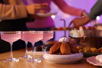 Glasses of cocktails and people with delicious desserts at buffet table, selective focus