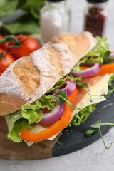 Delicious ciabatta sandwich with prosciutto, cheese and vegetables on light table, closeup