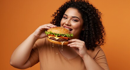 Woman is biting into large, juicy hamburger on orange background. Fast food burger