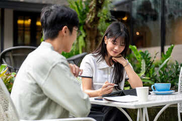 Glasses asian man looking at woman student with tablet doing an assignment at table in cafe's garden