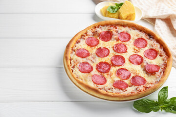 Delicious pepperoni pizza and ingredients on white wooden table. Space for text